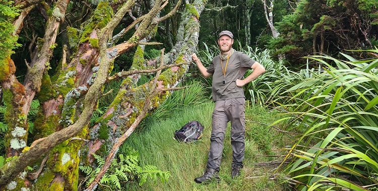 Onderzoeker Tim Claerhout staat in de natuur naast een mest mos begroeide boom